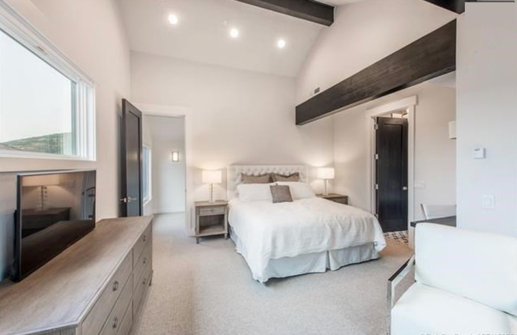 Second bedroom — vaulted ceiling, dark beam, tufted king bed