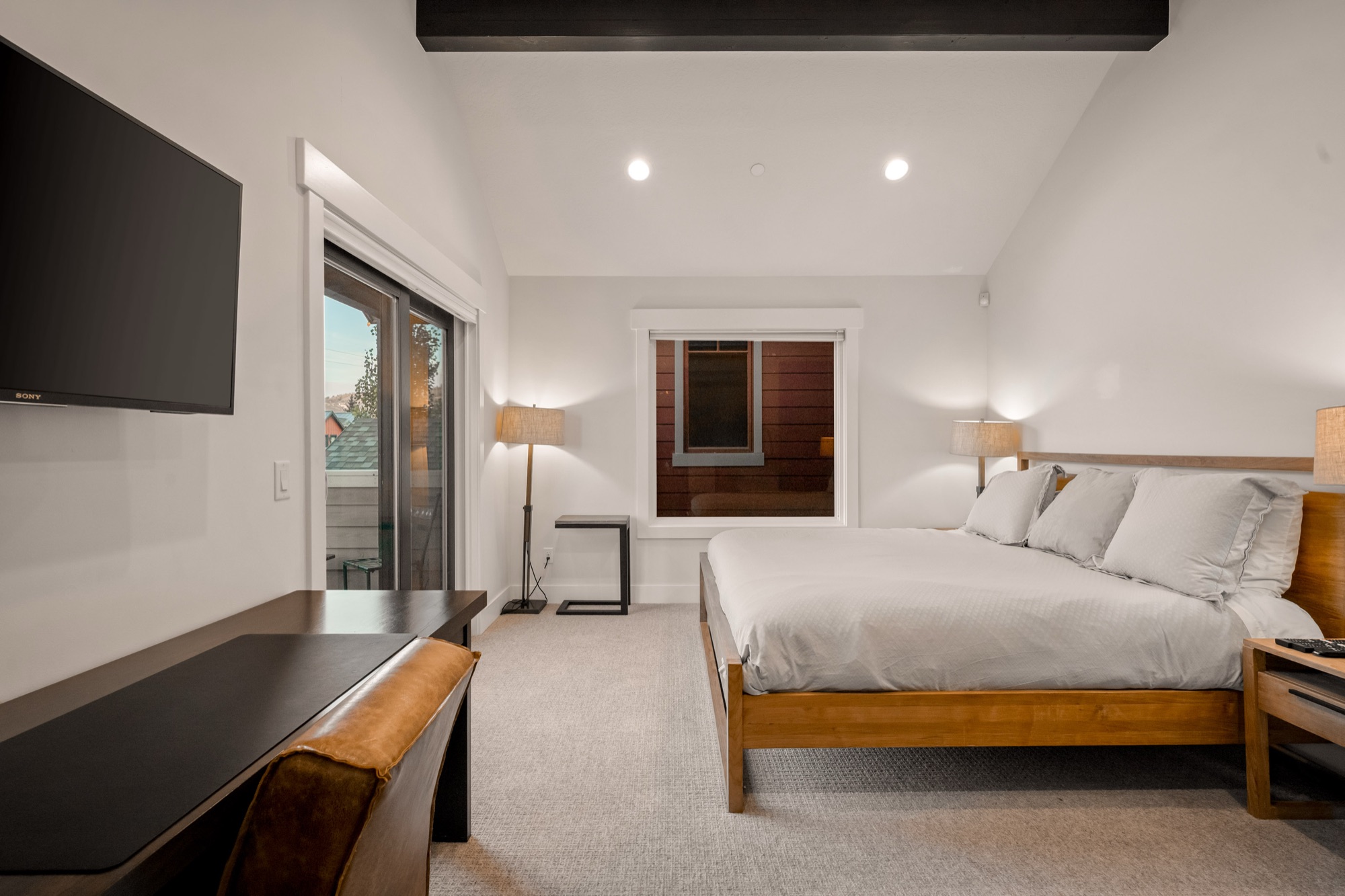 Second bedroom — vaulted ceiling, dark beam, tufted king bed